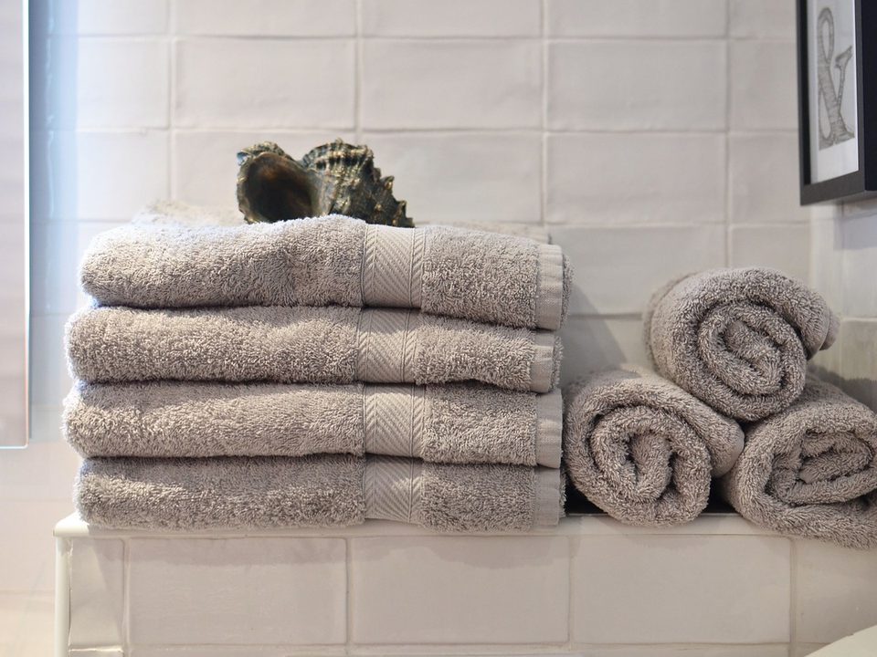 Stacked and rolled neutral bath towels in a tiled bathroom